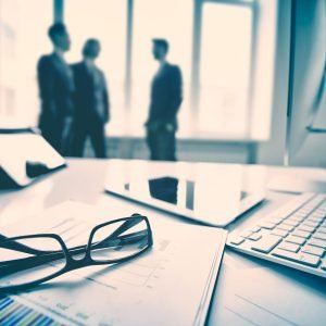 Modern devices, documents, eyeglasses on the foreground, unrecognized businessmen on the background
